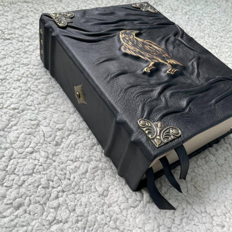 Pu&ograve; includere: Diario rilegato in pelle nera con un'aquila in rilievo e dettagli decorativi agli angoli. Il diario presenta una chiusura a fermaglio e segnalibri a nastro neri. La copertina ha un design in rilievo strutturato.