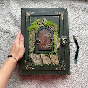 May include: A dark green leather-bound journal with a decorative wooden door design on the cover. The door is framed with moss, bark, and ornate metal accents. A lock and key secure the journal.