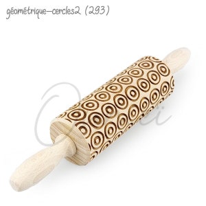 Puede incluir: Un rodillo de madera con un patrón de círculos concéntricos tallados en la superficie. El rodillo está hecho de madera clara y tiene un acabado natural.