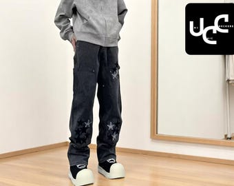 May include: Dark gray corduroy pants with embroidered star designs. The pants have a relaxed fit and are paired with white and black shoes. A gray hoodie is also visible. The image includes a logo that says "Unchecked Chic".