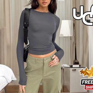 May include: A grey long-sleeved shirt with a fitted silhouette. The shirt has a round neckline and long sleeves. The model is wearing the shirt with olive green cargo trousers.