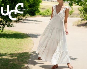 May include: A white tiered maxi dress with a V-neckline and ruffle straps. The dress is made of a lightweight fabric and has a flowy silhouette.