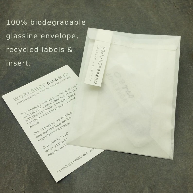 May include: A white, biodegradable glassine envelope with the text "WORKSHOP one80" printed on the front. The text "reclaim, sustain" is printed below the logo. The envelope is made from recycled materials and is designed to be eco-friendly.
