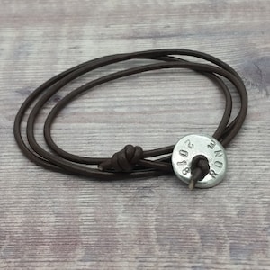 May include: A brown leather bracelet with a silver metal charm. The charm has the text "ROM 2018" engraved on it.