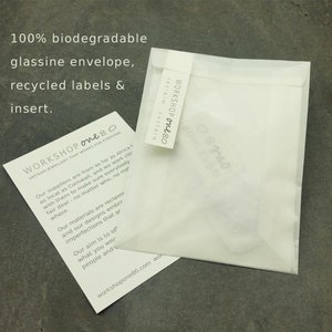 May include: A white, biodegradable glassine envelope with the text "WORKSHOP one80" printed on the front. The text "reclaim, sustain" is printed below the logo. The envelope is made from recycled materials and is designed to be eco-friendly.