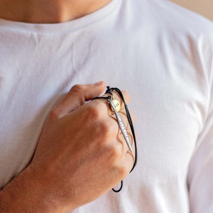 May include: A silver pendant necklace with a small round tag that says "118" and a long, thin, silver pendant with the word "SURVIVE" engraved on it. The necklace is on a black cord.