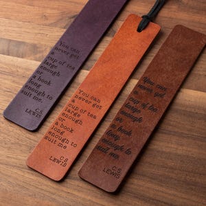 May include: Three leather bookmarks in shades of purple, orange, and brown, each with the quote "You can never get a cup of tea large enough or a book long enough to suit me" by C.S. Lewis. A black cord is attached to one bookmark.