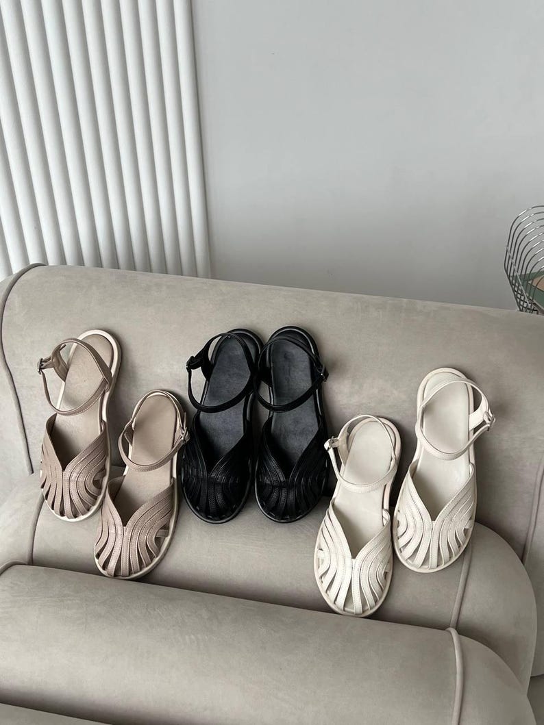 May include: Three pairs of closed-toe sandals in beige, black, and white. Each sandal features a woven, cage-like upper design with multiple thin straps, a rounded toe, and an adjustable ankle strap with a small metal buckle closure.