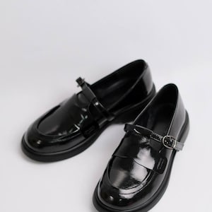 May include: Pair of black leather loafers with a buckle strap. The loafers have a rounded toe and a low heel.