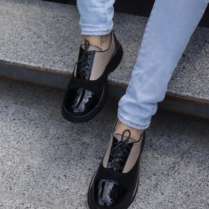 Puede incluir: Zapatos Oxford negros y beige con puntera negra brillante y cordones negros. Los zapatos tienen una suela negra gruesa y se usan con vaqueros azul claro. Dise&ntilde;o cl&aacute;sico con un toque moderno.
