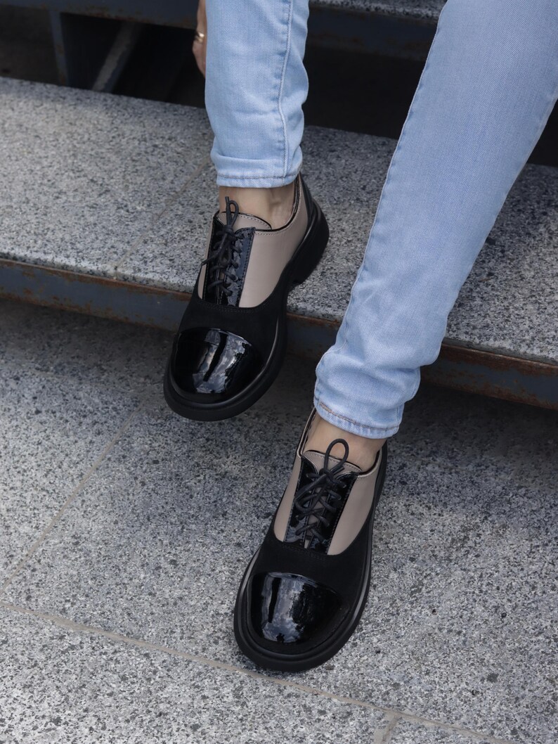 Puede incluir: Zapatos Oxford negros y beige con puntera negra brillante y cordones negros. Los zapatos tienen una suela negra gruesa y se usan con vaqueros azul claro. Dise&ntilde;o cl&aacute;sico con un toque moderno.