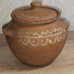 Puede incluir: Una olla de cocina rústica de barro con tapa. La olla es de color marrón cálido, adornada con patrones decorativos pintados de blanco. Cuenta con dos asas laterales y un pomo en la tapa. Una pieza encantadora para la decoración de la cocina.