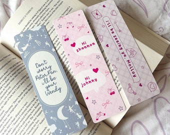 May include: Three pink and blue bookmarks with different designs and text. The bookmarks feature hearts, stars, bows, and cherries. The text on the bookmarks reads "Don't worry Peter Pan, I'll be your Wendy", "Hi Shannon", "Hi Johnny", and "I'll be seeing you Molly".