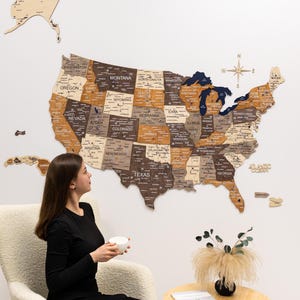 May include: A large wooden wall map of the United States featuring individual states in varying shades of brown, tan, and cream. The map includes labels for states, major cities, and the Great Lakes in dark blue, with a compass rose in the upper right.