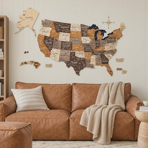 May include: A large wooden wall map of the United States featuring individual states in varying shades of brown and tan, with Alaska and Hawaii as separate pieces. The map includes a compass rose and text labels for states and oceans.