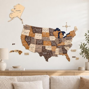 May include: A large wooden wall map of the United States featuring individual states in varying shades of brown, tan, and cream. The map includes Alaska and Hawaii as separate pieces, a compass rose, and labels for the Pacific and Atlantic Oceans.