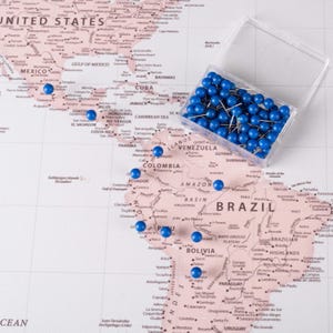 May include: A world map with blue push pins marking locations in Central and South America. The pins are in a clear plastic container.