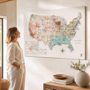 May include: A large rectangular wall map of the United States featuring a watercolor-style color gradient across the states, with black text labels for cities and regions, a compass rose, and inset maps of Alaska and Hawaii on a white background.
