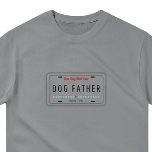 Puede incluir: Camiseta gris de manga corta con un gráfico de una placa de matrícula que dice "Dog Father" con el texto "Best Dog Dad Ever" arriba.