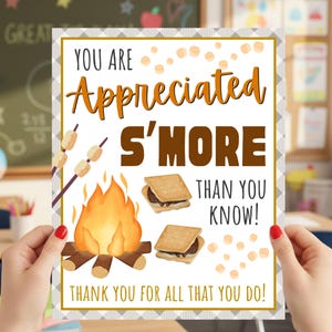 May include: A rectangular print with the text "YOU ARE Appreciated S'MORE THAN YOU KNOW! THANK YOU FOR ALL THAT YOU DO!" features a campfire, marshmallows, and s'mores. The print is held in front of a classroom setting.
