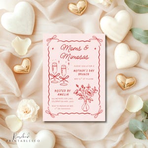 May include: A pink invitation card with red text and illustrations. The text reads "Moms & Mimosas" and "Please join us for a Mother's Day Brunch, May 12th at 11:00am". The illustration shows two champagne glasses and a vase of flowers.