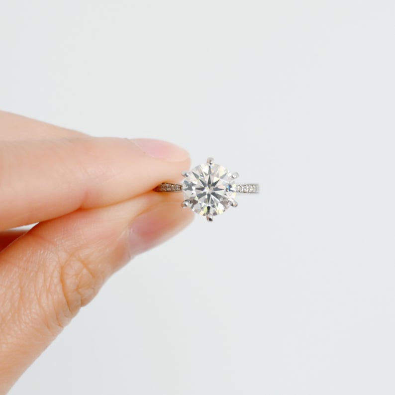 K&ouml;nnte beinhalten: Ein silberner Ring mit einem gro&szlig;en, runden, klaren Diamanten in der Mitte und einer kleineren Diamantfassung.