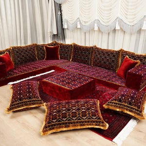 May include: A burgundy sectional sofa set with patterned cushions and pillows. The set includes a corner sofa, an ottoman, and several throw pillows. The cushions and pillows have gold accents, creating a luxurious and inviting space for relaxation.