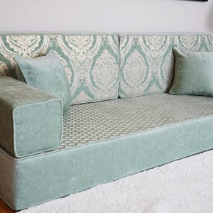 May include: A mint green modular sofa with two square armrests and two matching throw cushions. The back of the sofa features a damask pattern in white and mint green. The seat cushion has a subtle geometric pattern.