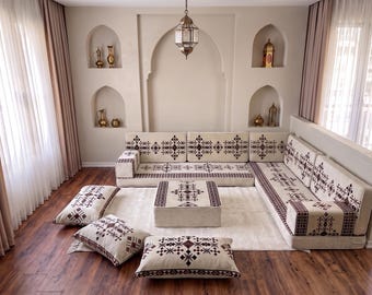 May include: An L-shaped floor sofa set with a cream-coloured fabric featuring a dark brown geometric pattern. The set includes a low-profile sectional sofa, a matching square ottoman, and three rectangular floor cushions, all with identical motifs.