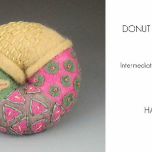 May include: A donut-shaped needle felted brooch with a pink, green, and beige design. The brooch is made with wool and has a variety of textures. The text "DONUT BROOCHES" and "Intermediate Needle Felting with HARLAN" is visible in the image.