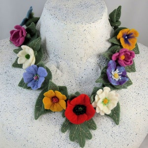 Puede incluir: Un collar de flores de fieltro con una variedad de colores, incluyendo rojo, blanco, azul, amarillo y rosa. El collar está hecho de flores y hojas de fieltro, y está enhebrado con un hilo.