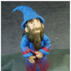 Puede incluir: Un muñeco de mago de fieltro azul con una larga barba marrón, que lleva un sombrero azul y una túnica roja y azul, sosteniendo un palo rojo y negro.