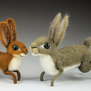 May include: Three felted rabbit figurines, one brown, one gray, and one gray with white accents. The rabbits are posed in a playful, energetic manner.