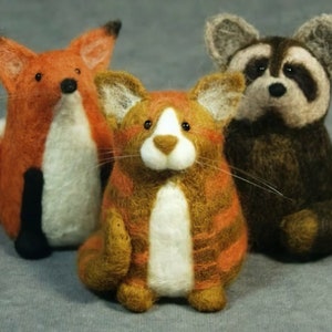 May include: Three felted animal toys: a red fox, a brown raccoon, and a brown and white tabby cat.