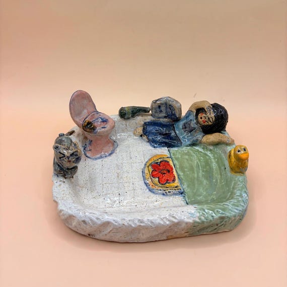 A handmade ceramic soap dish sculpted as a tiny toilet scene — equal parts absurdist humor and actually functional bathroom art.