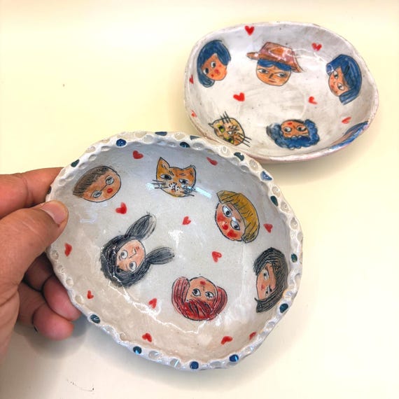 A hand-illustrated ceramic dish featuring quirky 'Loveheads' faces — original character art fired into clay makes this genuinely one-of-a-kind.