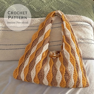 May include: A crochet bag featuring a wavy, vertical striped pattern in mustard yellow, cream, and light brown yarn. The bag has a single integrated handle and a small, smooth, oval-shaped wooden toggle button centred at the top opening.