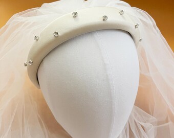 May include: A white satin headband with a row of clear rhinestones. The headband is on a white mannequin head with a white tulle veil.