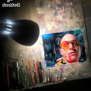 May include: A close-up of a drawing of a man with a cigarette in his mouth, wearing sunglasses and a yellow shirt. The drawing is on a white background and is surrounded by art supplies, including pencils, erasers, and cotton swabs.