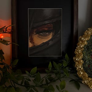 May include: A framed artwork featuring a detailed eye peering out from a dark, shadowed space. The painting uses a palette of blacks, browns, and reds, with the eye as the focal point. The frame is dark brown.