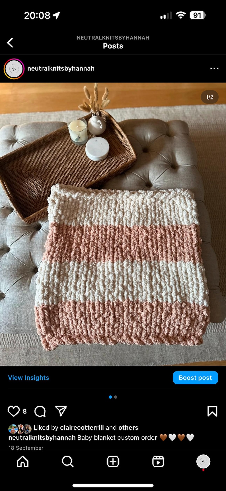 May include: A pink and white striped chunky knit baby blanket. The blanket is on a light grey ottoman with a woven tray and candles on top.