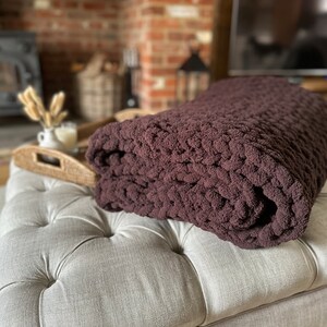 May include: A brown chunky knit throw blanket folded on a light grey tufted ottoman.