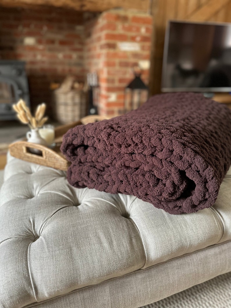 May include: A brown chunky knit throw blanket folded on a light grey tufted ottoman.