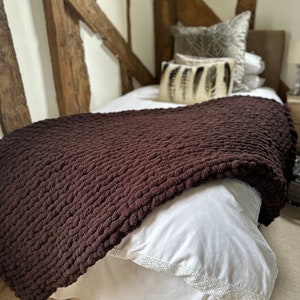 May include: A brown chunky knit throw blanket on a white bed with a white bed skirt. The bed has two pillows with a feather pattern on them.