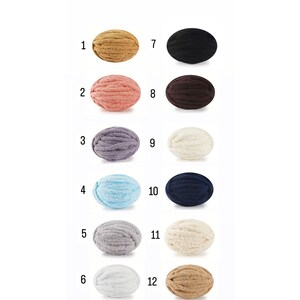 May include: Twelve balls of yarn in various colours, including beige, pink, grey, blue, white, and black. The balls are arranged in two rows of six, with numbers 1 through 12 labelling each ball.