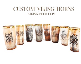 May include: A collection of Viking horn beer cups with gold rims and various etched designs. The cups are made of natural horn material, showcasing a range of colors from light beige to dark brown. The text "CUSTOM VIKING HORNS VIKING BEER CUPS" is displayed above the cups.