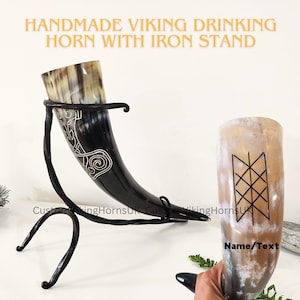 May include: A handmade Viking drinking horn with an iron stand. The horn is decorated with a black and white design. The stand is made of twisted metal.
