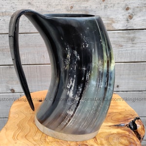 May include: A black and white drinking horn with a silver rim. The horn is on a wooden surface.