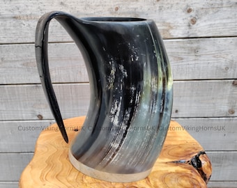 May include: A black and white drinking horn with a silver rim. The horn is on a wooden surface.