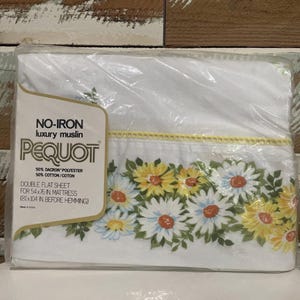 Puede incluir: Una sábana plana doble blanca empaquetada con un estampado floral de margaritas. La sábana está etiquetada como "Pequot" y "No-Iron luxury muslin". La sábana está diseñada para un colchón de 137x193 cm.